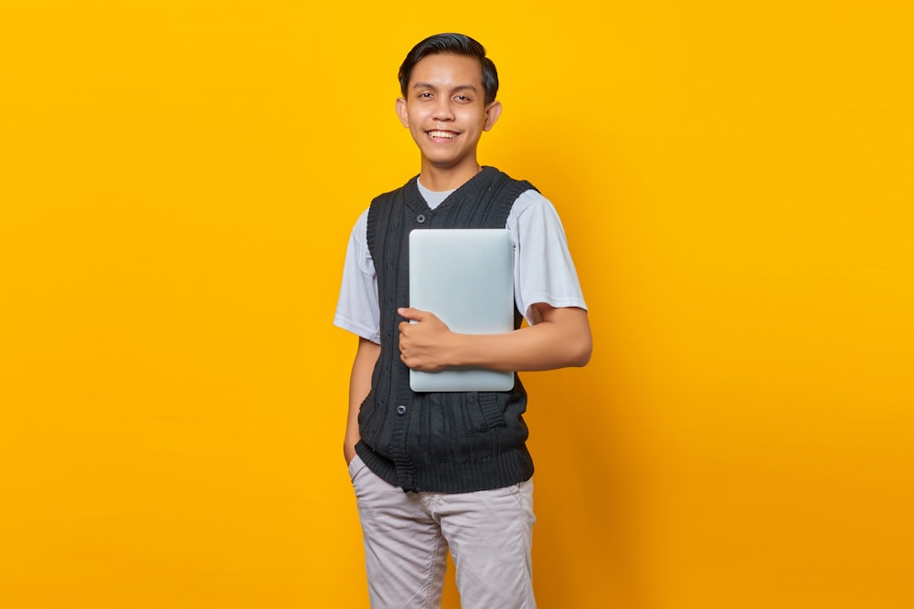 a young man holding a laptop on a yellow background