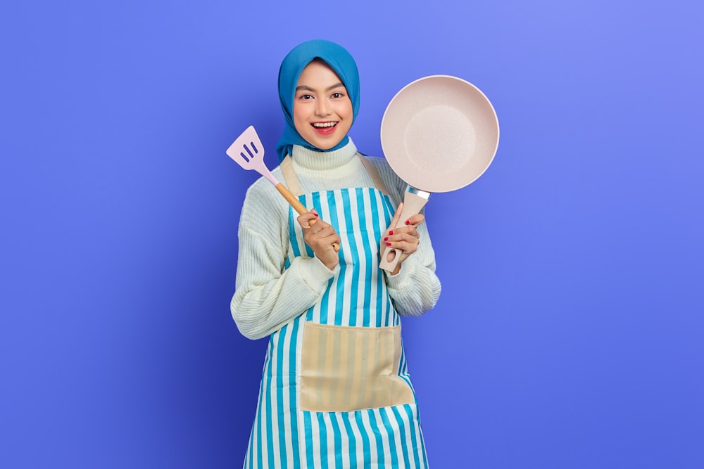 a woman in an apron holding a spatula and a frying pan