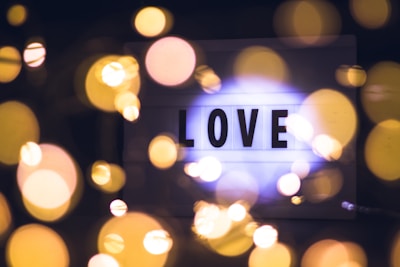 A lightbox with the word 'LOVE' illuminated against a dark background, surrounded by out-of-focus golden bokeh lights that create a dreamy and romantic atmosphere.