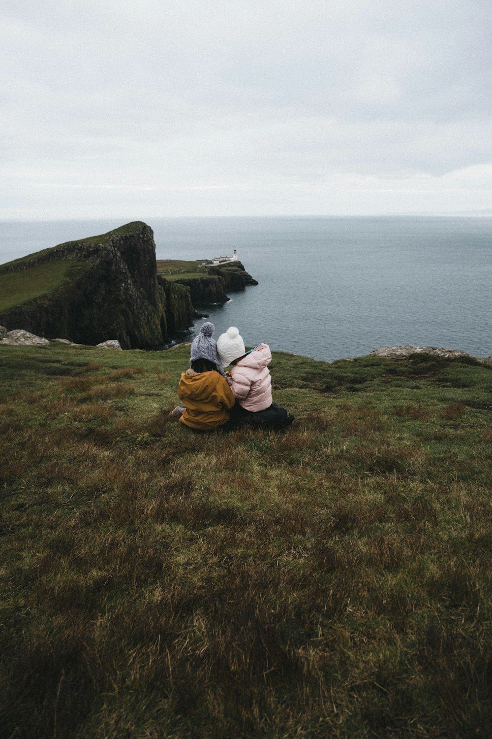 a couple of people sitting on top of a grass covered hill