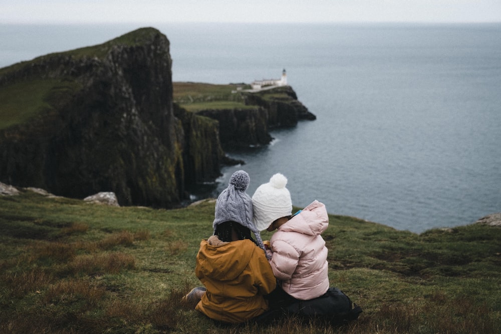 a couple of kids sitting on top of a grass covered field