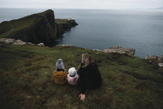 a woman and two children sitting on a hill overlooking a body of water