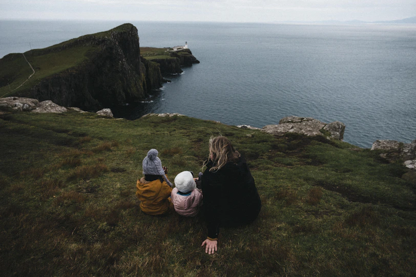 a woman and two children sitting on a hill overlooking a body of water