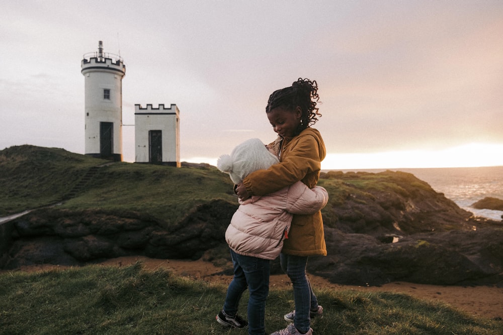 a woman holding a child near a lighthouse
