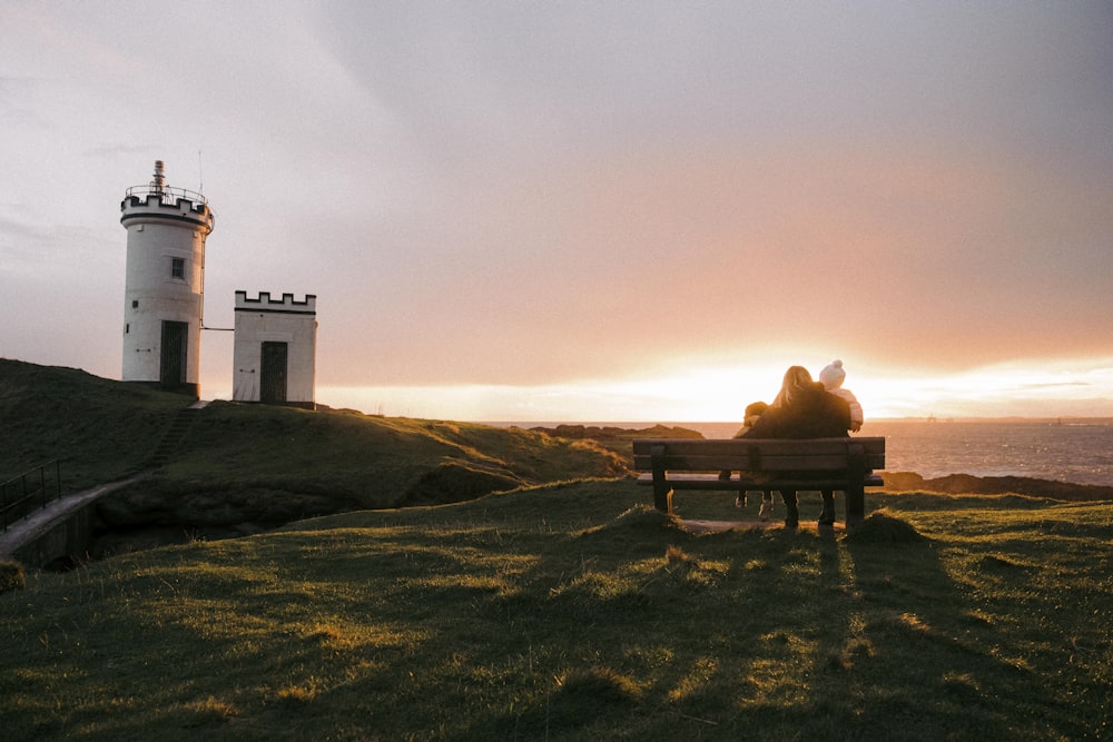 a couple sitting on a bench in front of a lighthouse