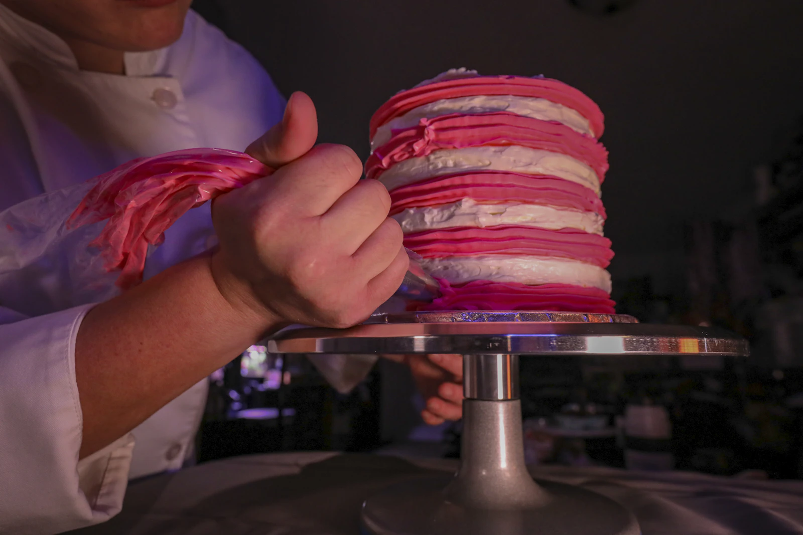 Baker piping custom buttercream decoration onto a designer cake, an example of made-to-order cake decorating