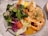A plate filled with a fresh salad, shrimp topped with garlic and herbs, and rice balls. The salad includes mixed greens, cherry tomatoes, and red cabbage. The shrimp are bright orange and surrounded by a sauce.