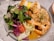 A plate filled with a fresh salad, shrimp topped with garlic and herbs, and rice balls. The salad includes mixed greens, cherry tomatoes, and red cabbage. The shrimp are bright orange and surrounded by a sauce.