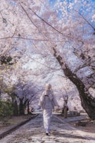 a woman walking down a road with lots of pink flowers
