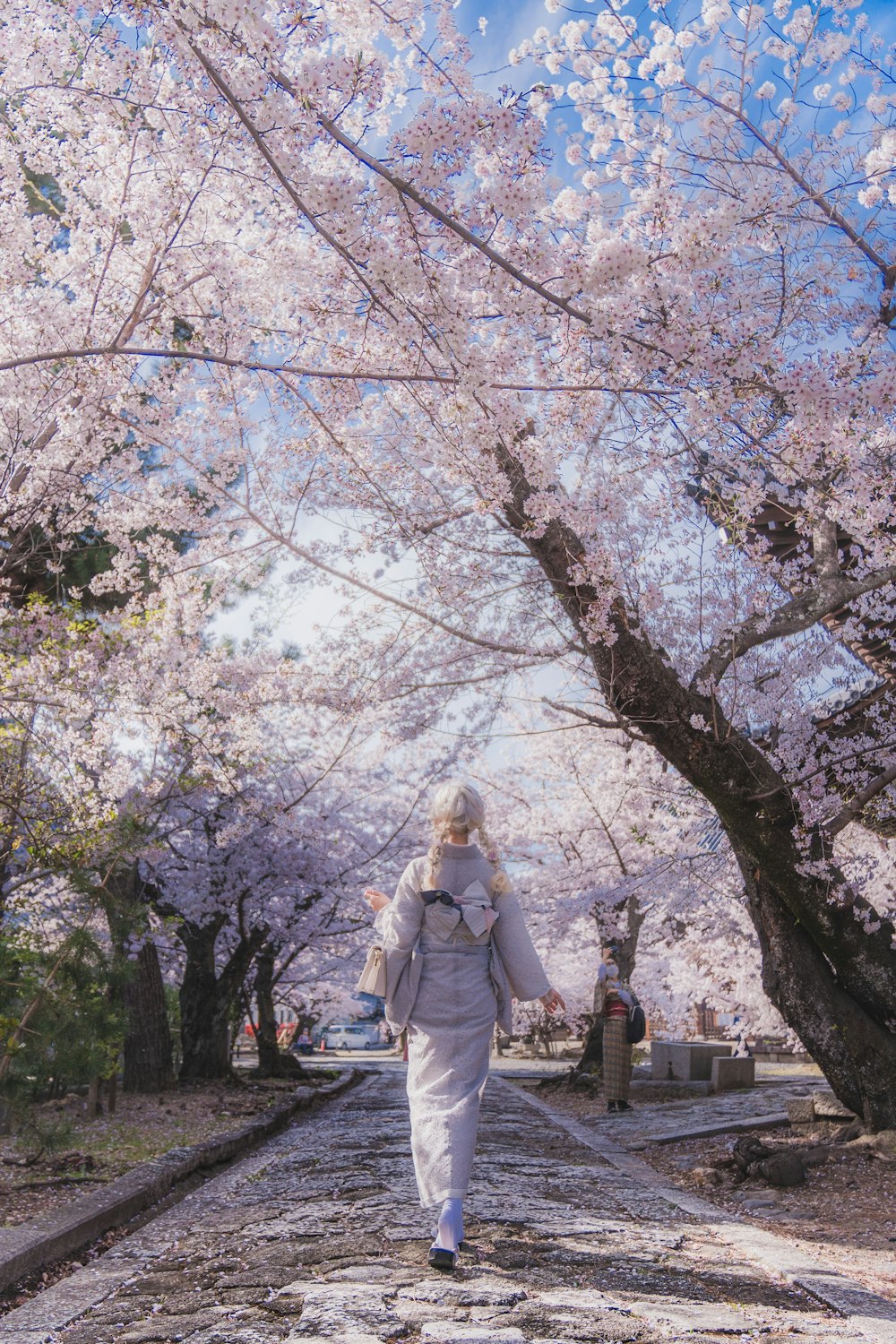 a woman walking down a road with lots of pink flowers