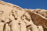 statues of pharaohs and queens in front of a rock formation