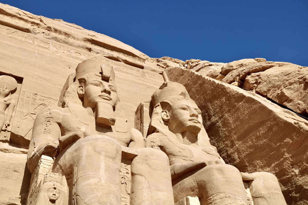 estátuas de faraós e rainhas em frente a uma formação rochosa
