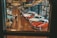 A well-lit showroom displays a collection of classic cars arranged in rows. Two people are examining one of the cars while several others walk around the exhibit. The setting includes reflective glass walls and a suspended vintage airplane, adding to the automotive theme.