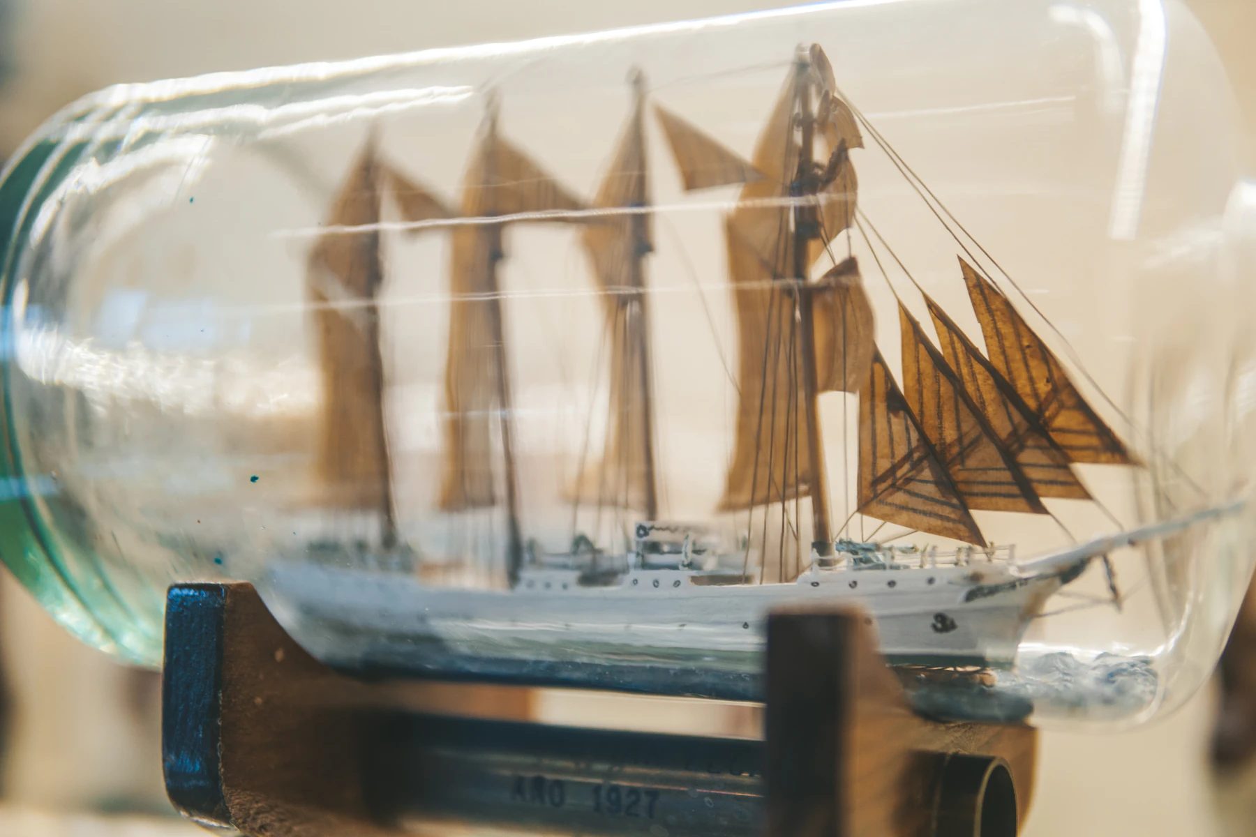 Close-up through bottle glass of a many-masted model schooner with brown sails and fine thread rigging