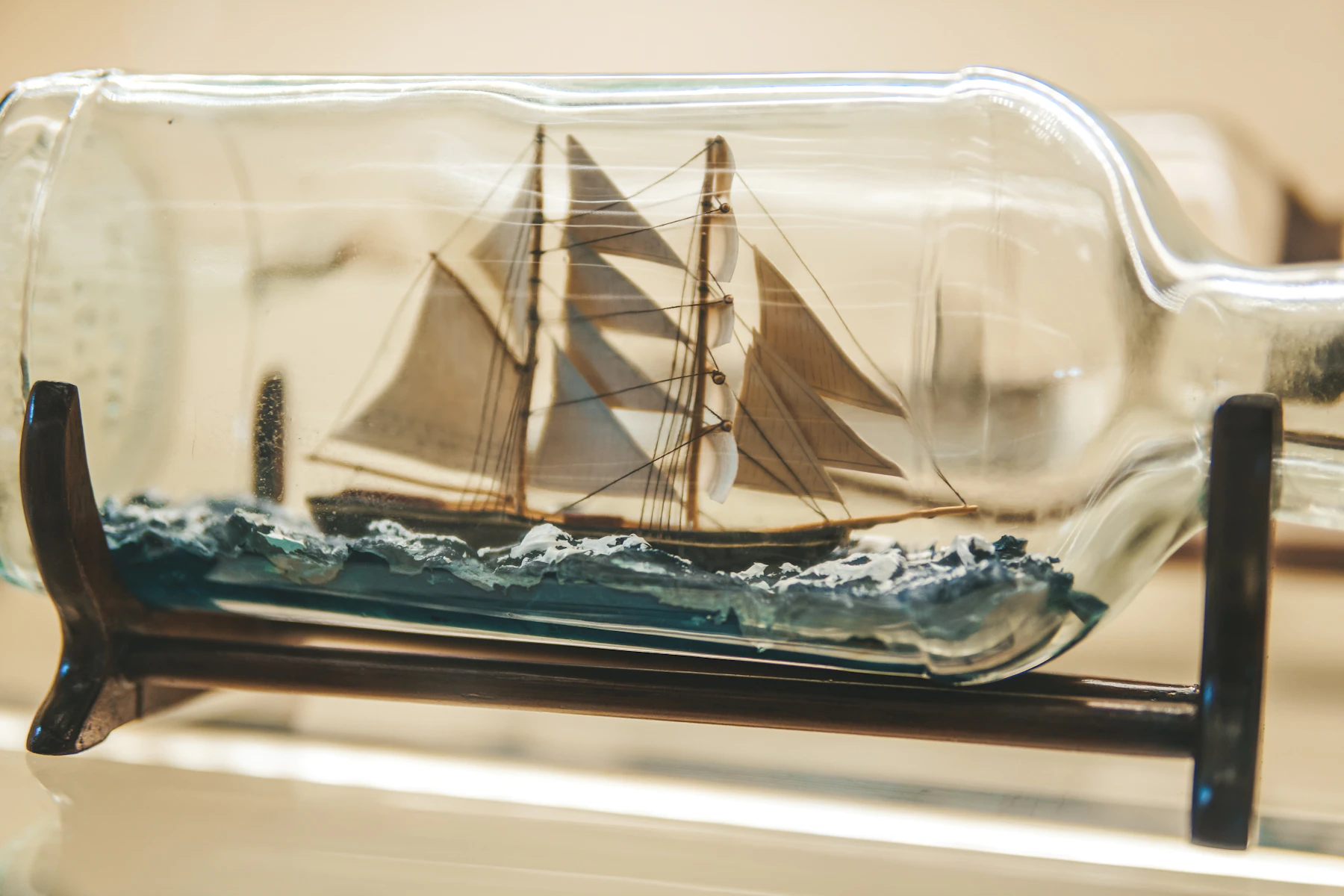 A model schooner on a molded blue sea inside a glass bottle lying on a wooden cradle