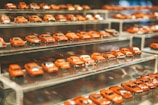 A collection of miniature red car models displayed on multiple clear, tiered shelves. The cars are neatly arranged in rows and are all similar in shade, creating a visually cohesive and organized appearance.