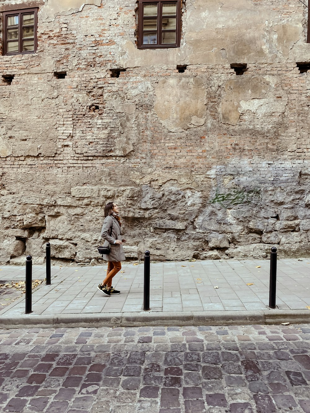 a woman walking down a sidewalk next to a stone building