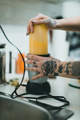 a woman is holding a blender with a tattoo on her arm