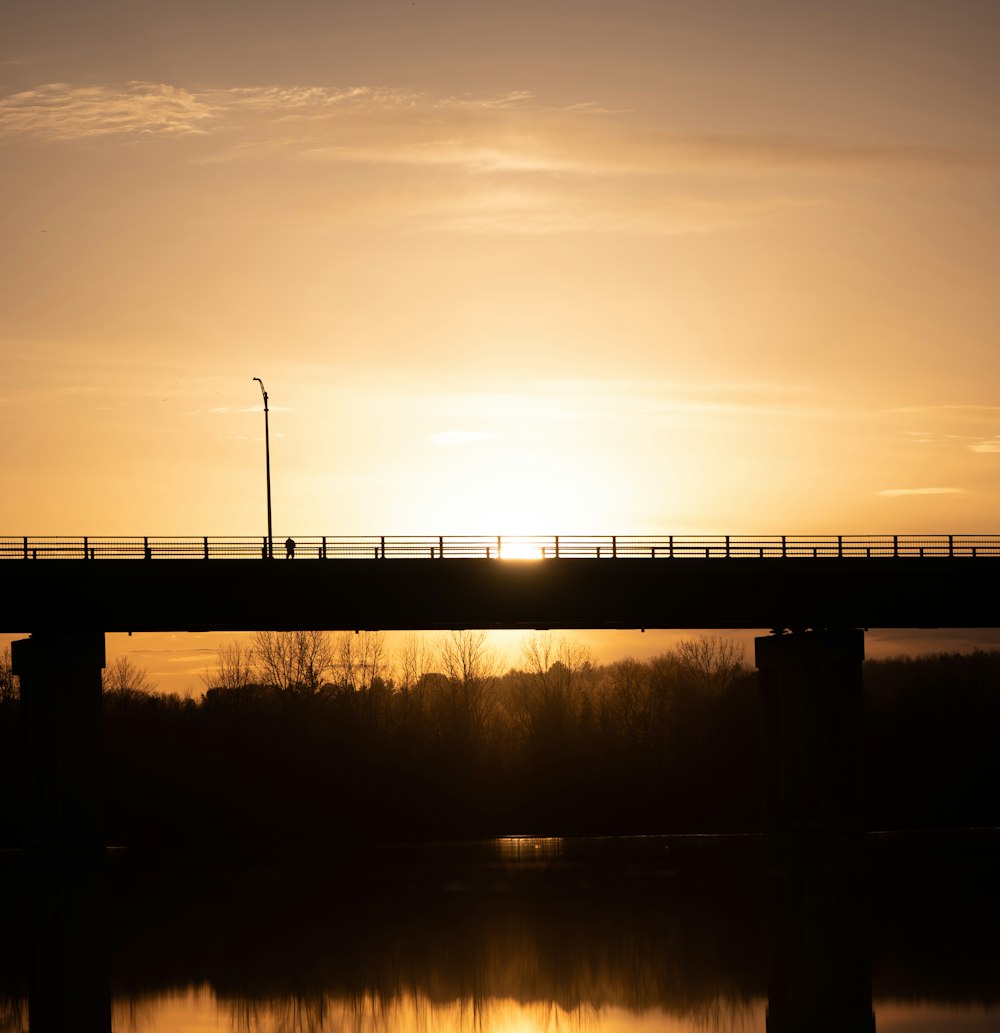 the sun is setting on a bridge over a body of water