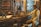 A workshop filled with a variety of vintage tools hanging on the wall. A mannequin dressed in vintage attire is seated, appearing as if working with the machinery on the wooden table. The workshop has a rustic feel with wooden shelves and brick walls.