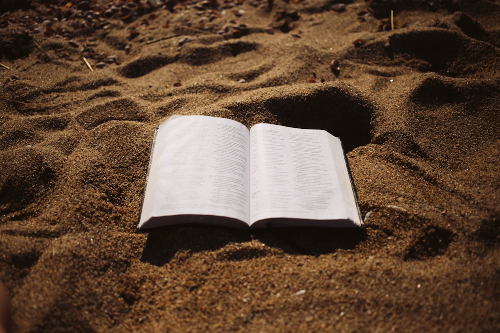 an open book sitting on top of a sandy beach