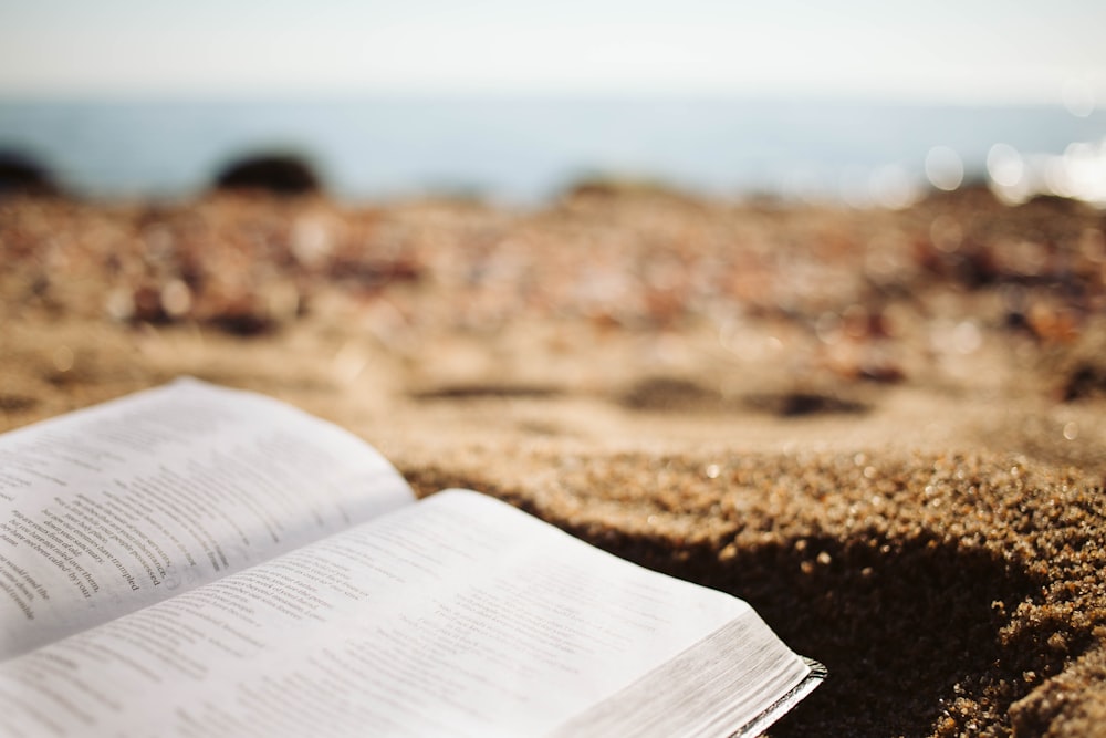 an open book sitting on top of a sandy beach