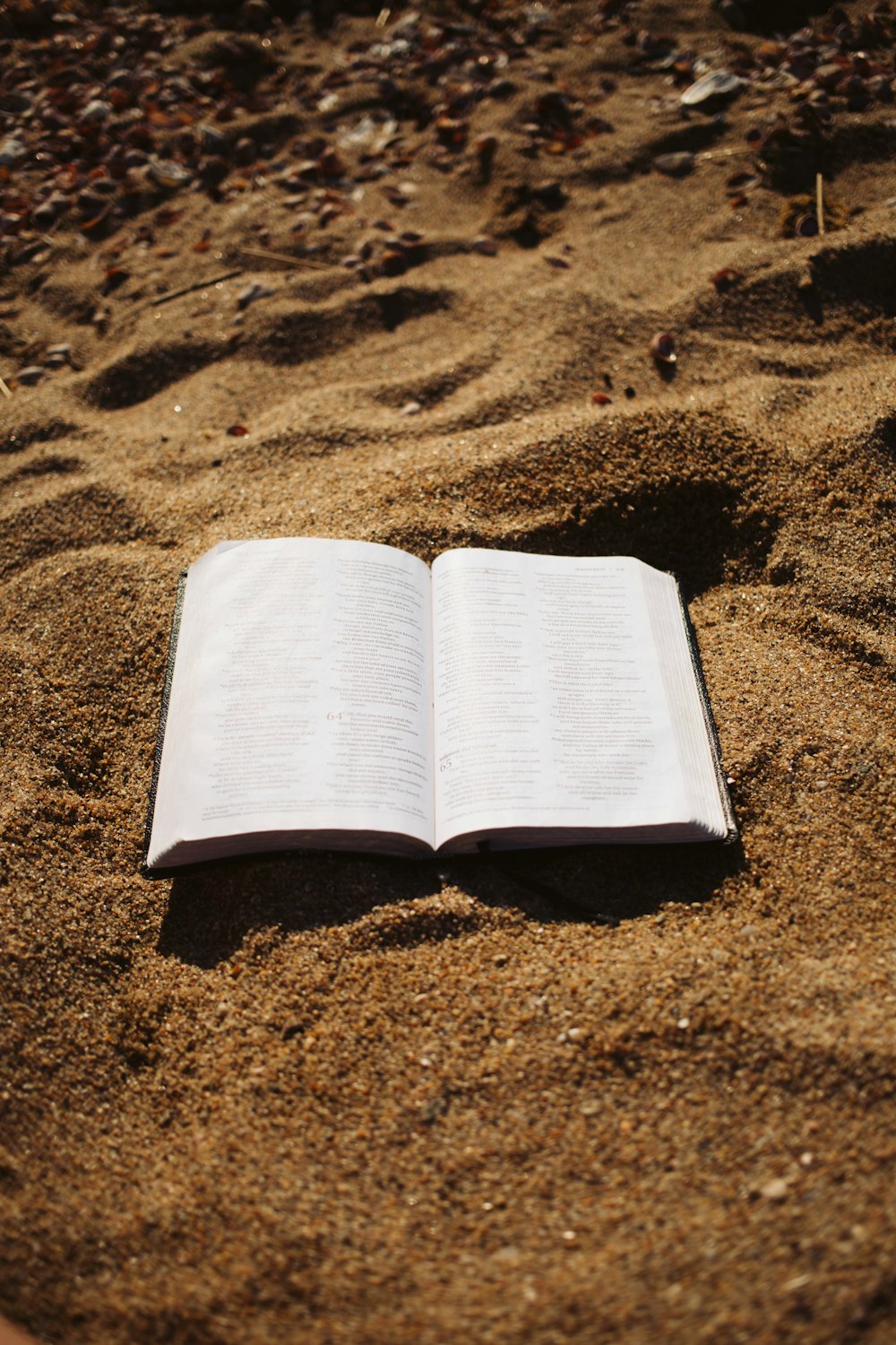 an open book sitting on top of a sandy beach