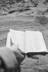 Close-up of hands holding an open book with charcoal text on soft sand background