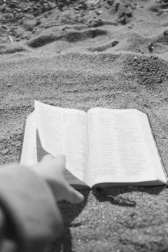 Close-up of hands holding an open book with charcoal text on soft sand background