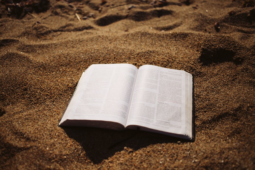 um livro aberto sentado em cima de uma praia de areia