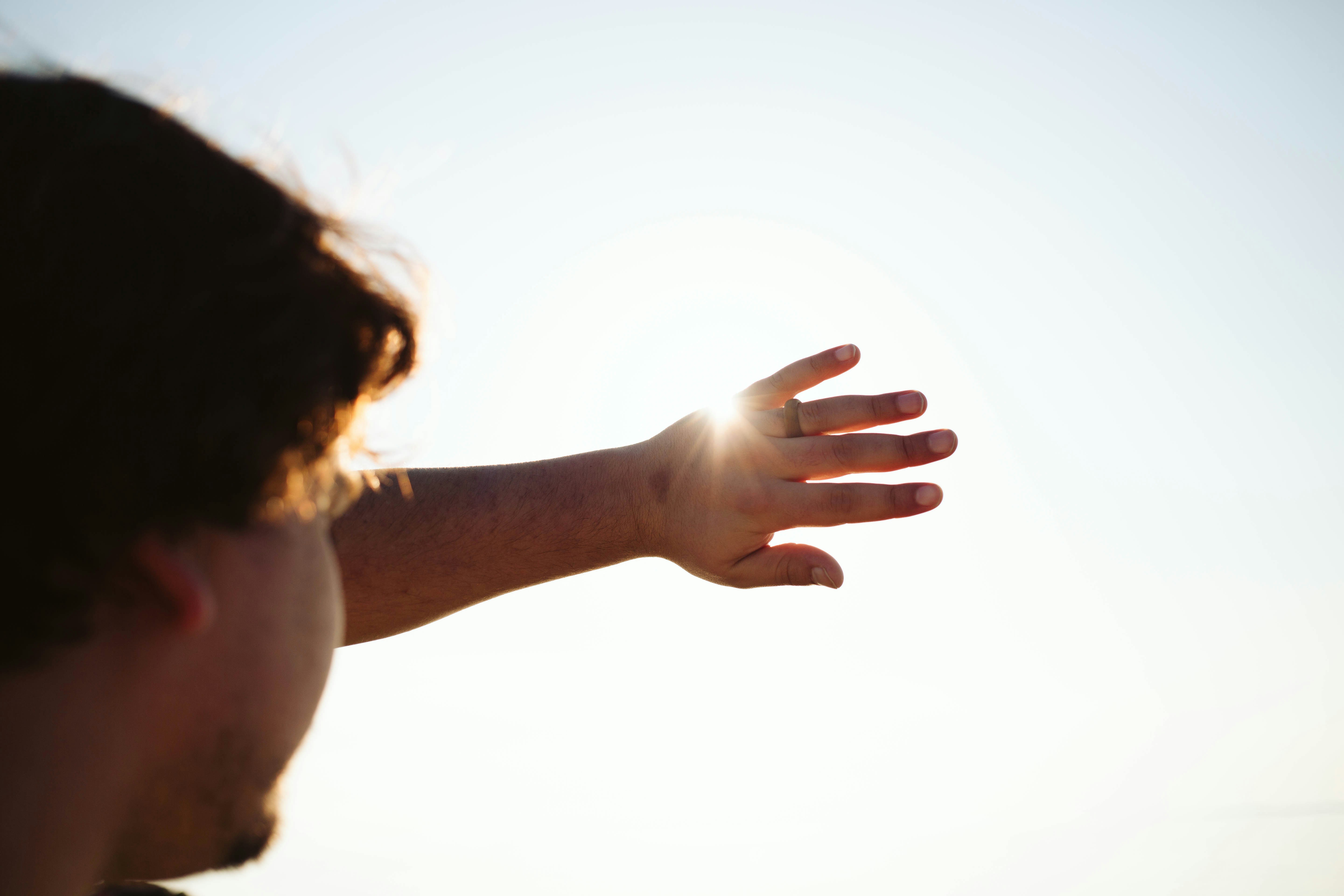 a man holding his hand out towards the sun