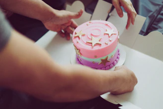 Close-up of hands carefully frosting a colorful cake, capturing the art and care behind each creation.