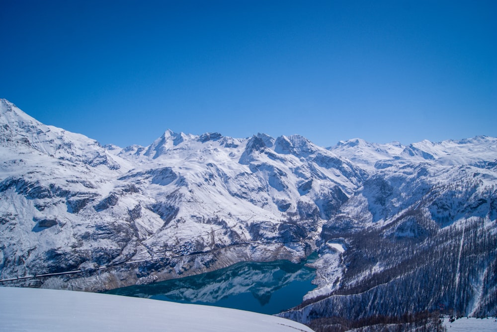 a snow covered mountain range with a lake in the foreground