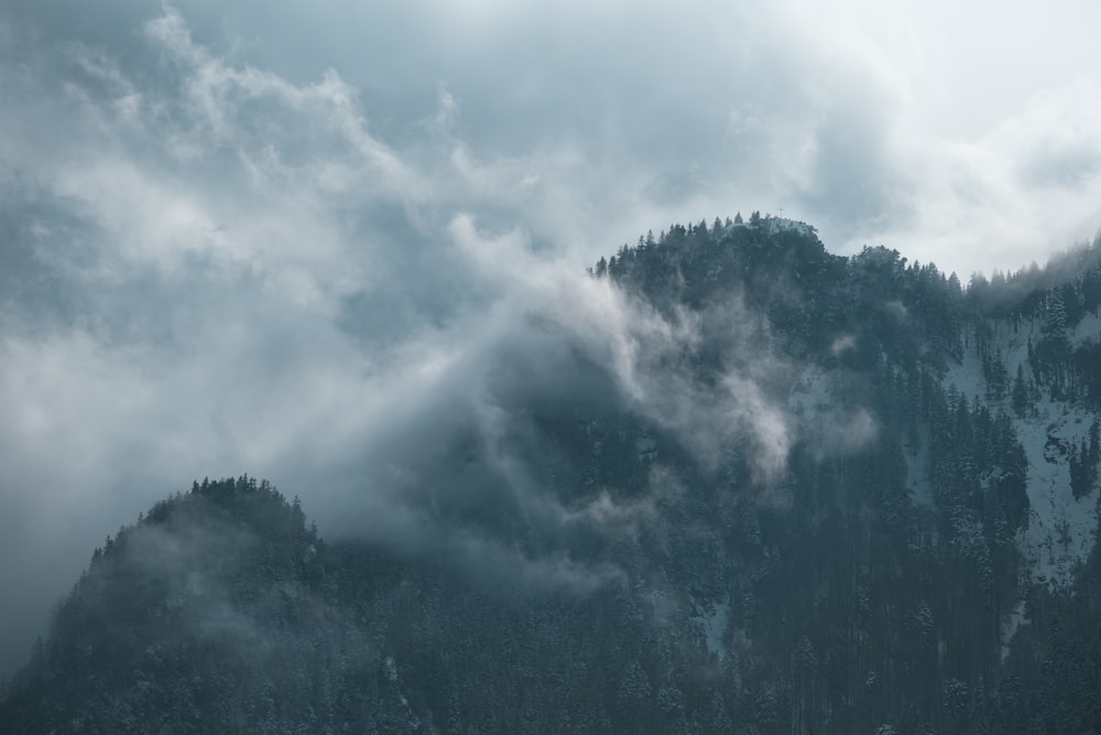 a mountain covered in clouds and trees under a cloudy sky