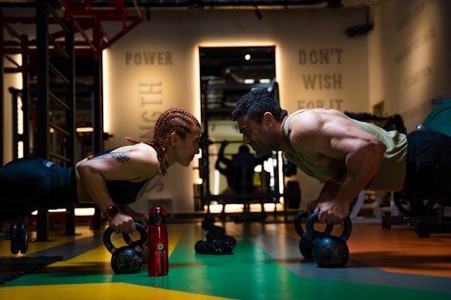 a man and a woman doing push ups with kettles