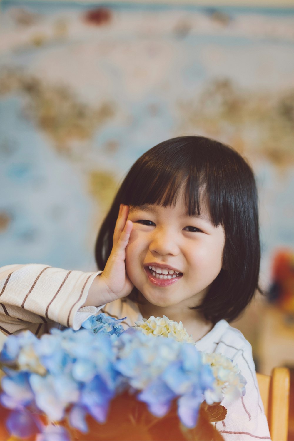 a little girl sitting at a table with blue flowers
