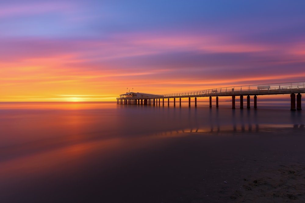 a long pier stretches out into the ocean as the sun sets