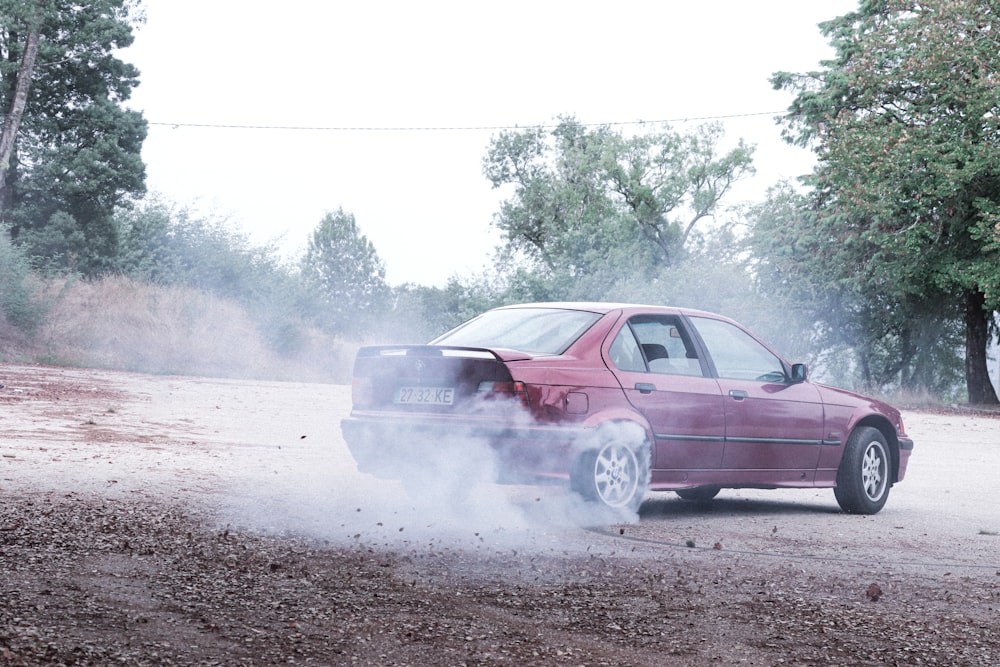 a red car driving down a dirt road next to a forest