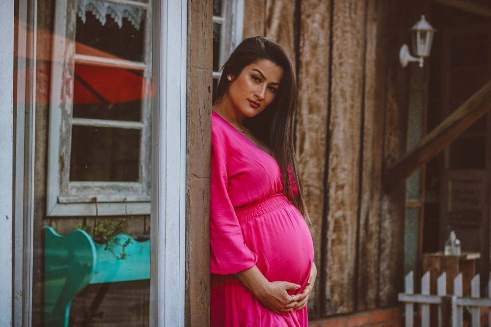 a pregnant woman in a pink dress leaning against a wall