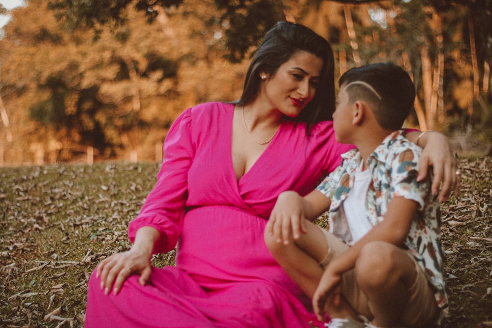 a woman in a pink dress sitting next to a little boy