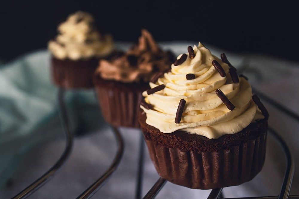 three cupcakes with white frosting and chocolate sprinkles