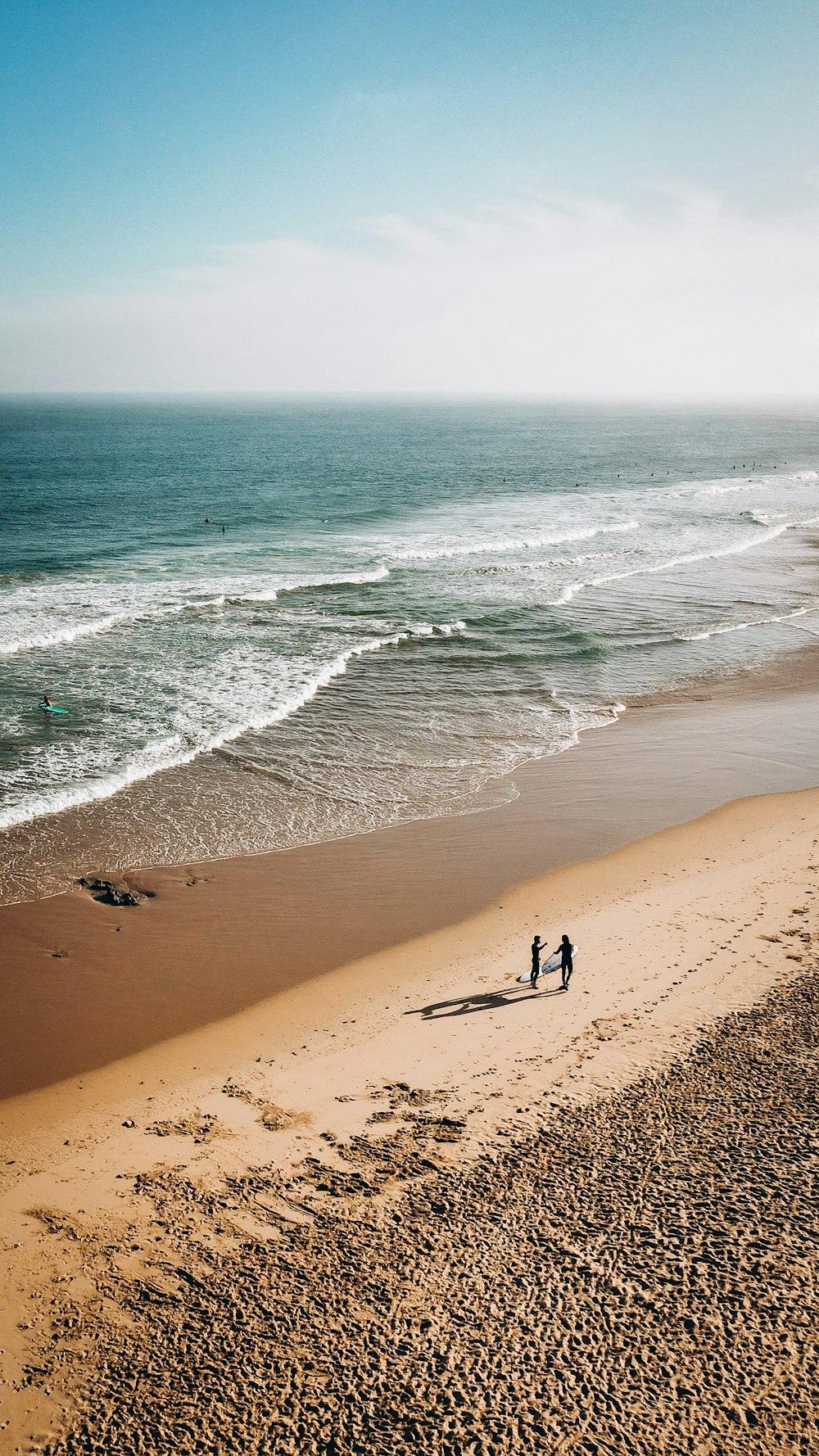 a couple of people walking along a beach next to the ocean