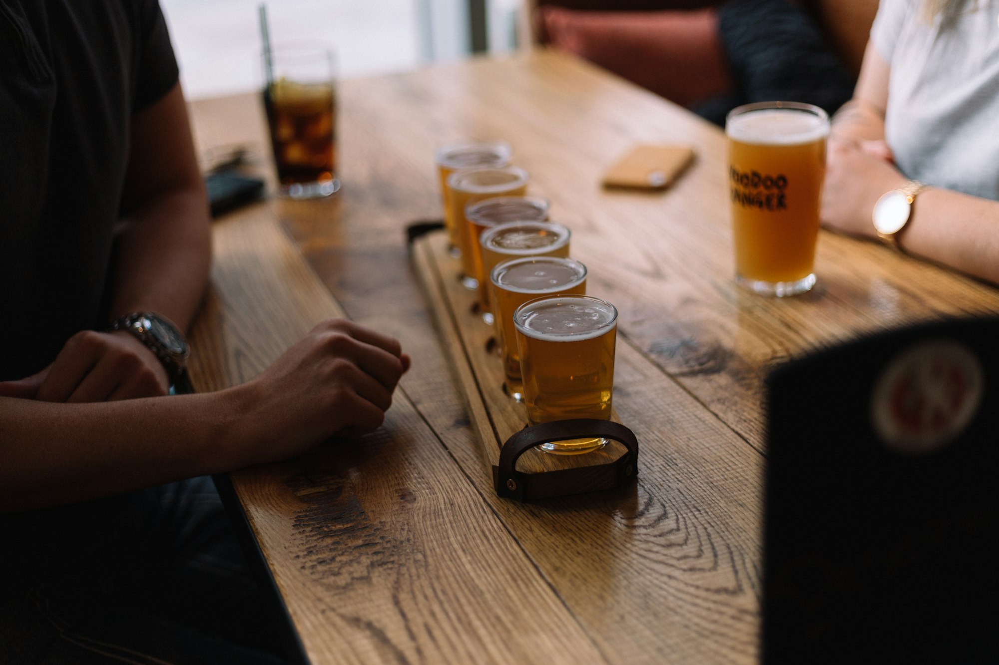 a group of people sitting around a wooden table drinking a flight of beer
