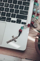 Close-up of hands typing on a laptop with a cross pendant resting nearby.