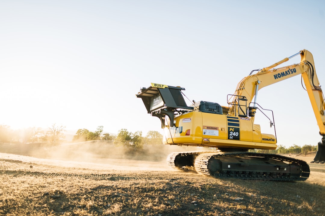 a yellow construction vehicle driving down a dirt road, A fully autonomous excavator tracks down a hill at sunset.