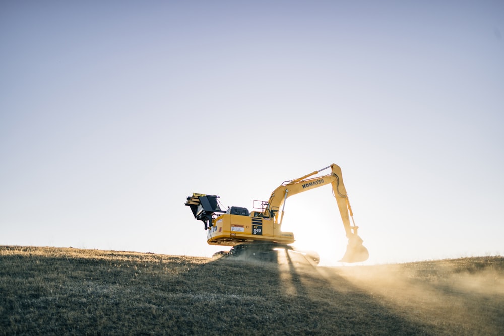 a yellow excavator on a hill with a blue sky in the background