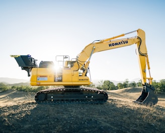 a yellow excavator sitting on top of a dirt field