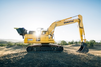 a yellow excavator sitting on top of a dirt field