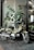 A motorcycle is parked on a tiled floor near a glass window. It has a green body with the label 'CC110' and 'Honda' visible. Behind the motorcycle, there is a large plant with broad leaves, and the window reflects a hair design shop with a visible name 'ANDALUZ'. The scene includes a mix of indoor and outdoor elements, with natural light illuminating the area.