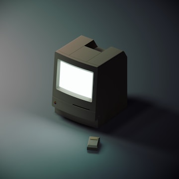 A vintage-style computer with a large off-white monitor is accompanied by a matching mouse. The scene is minimally lit, creating a soft, focused ambiance.